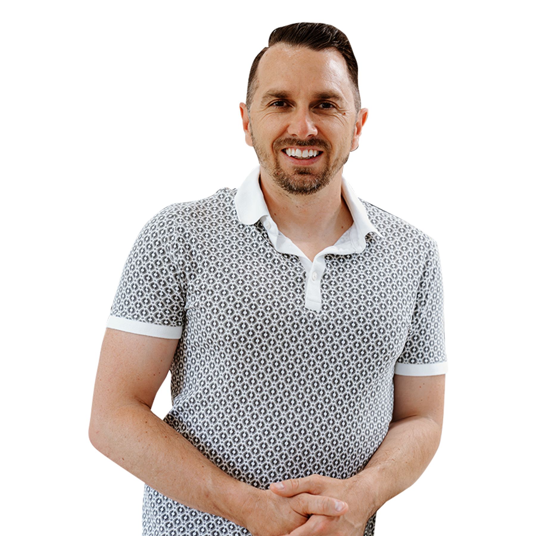 A smiling man with dark hair and a beard, wearing a patterned short-sleeve polo shirt, standing with hands clasped in front of him.