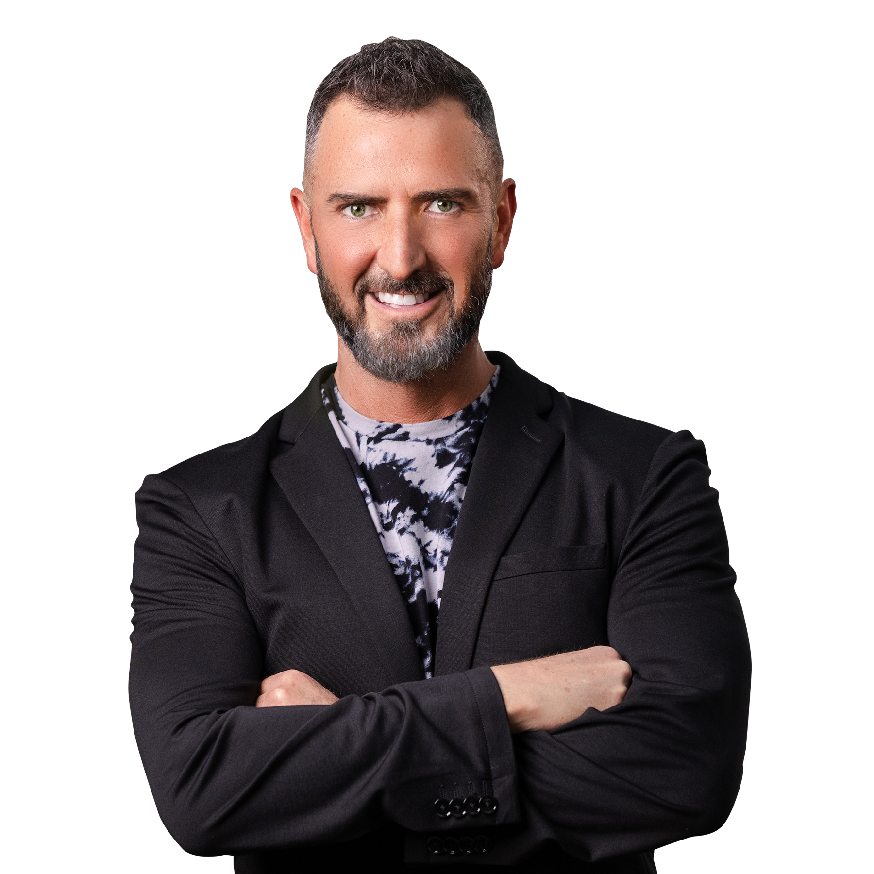 A smiling man with gray hair and beard, wearing a black blazer over a black and white tie-dye shirt, crossing his arms.